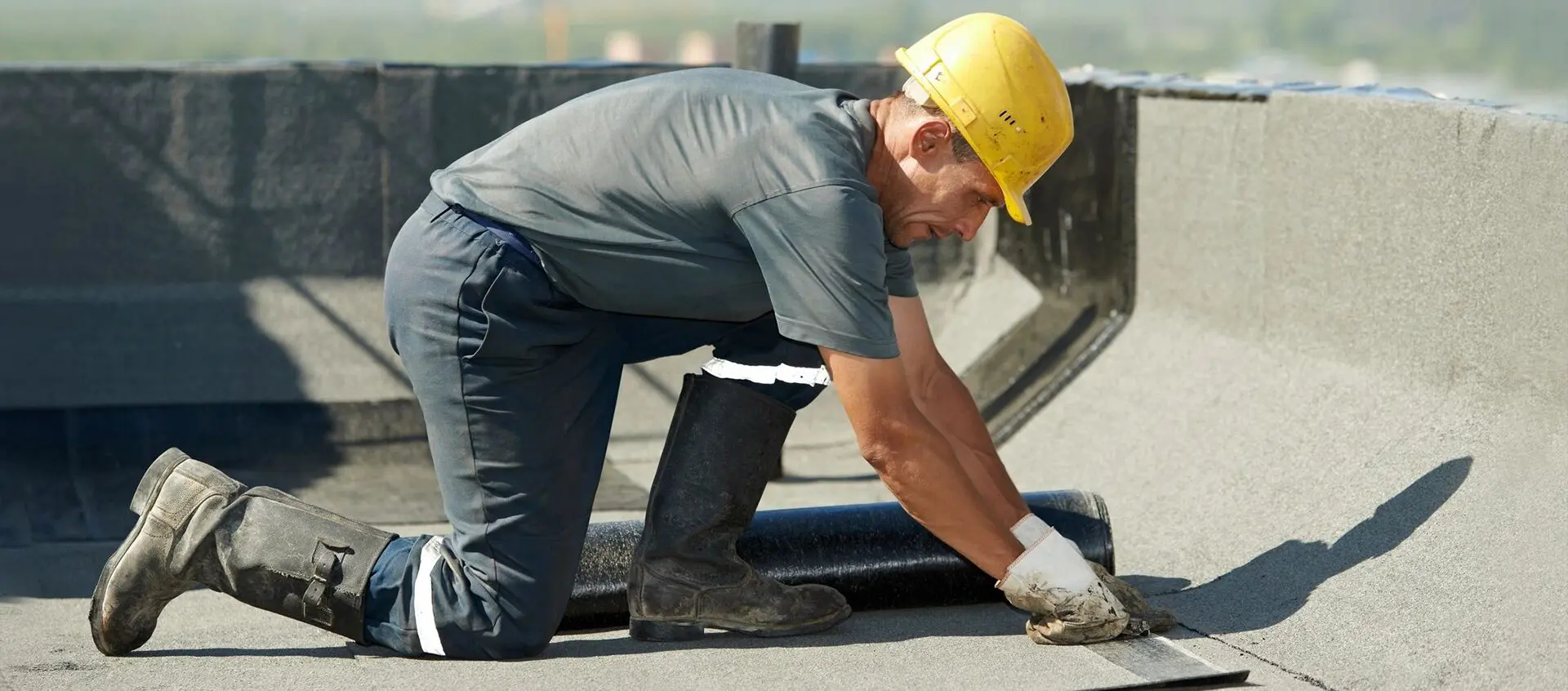 A man wearing a hard hat and gloves rolling a roll of water.