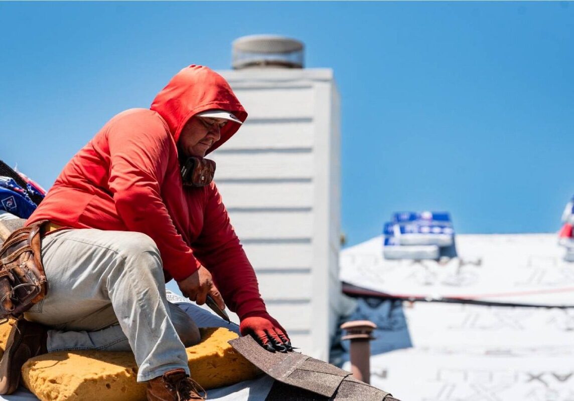 A man in a red hoodie is working on a roof.